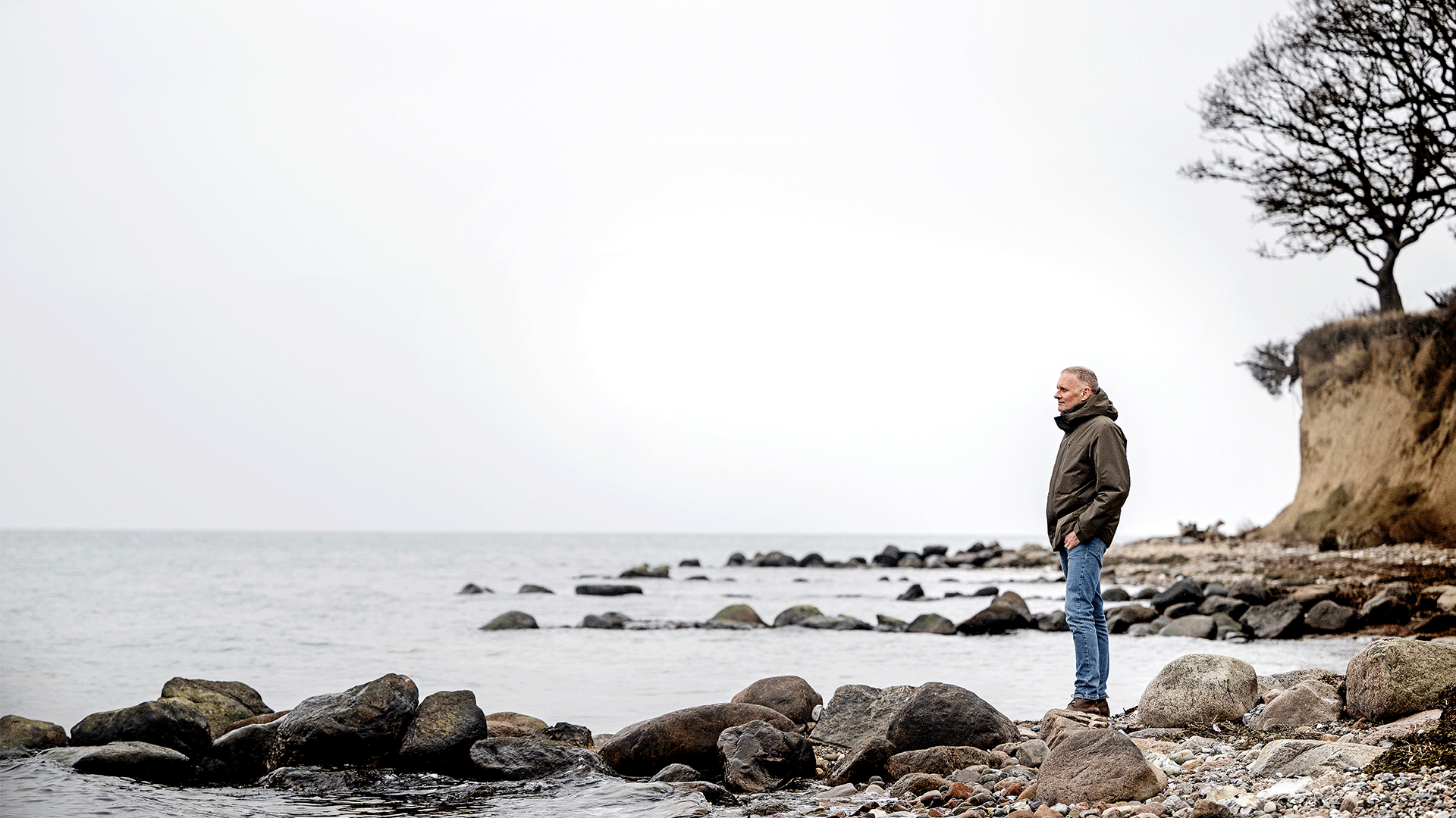 Professor Anders Baun standing on a beach beneath an outcrop looking out over the water.