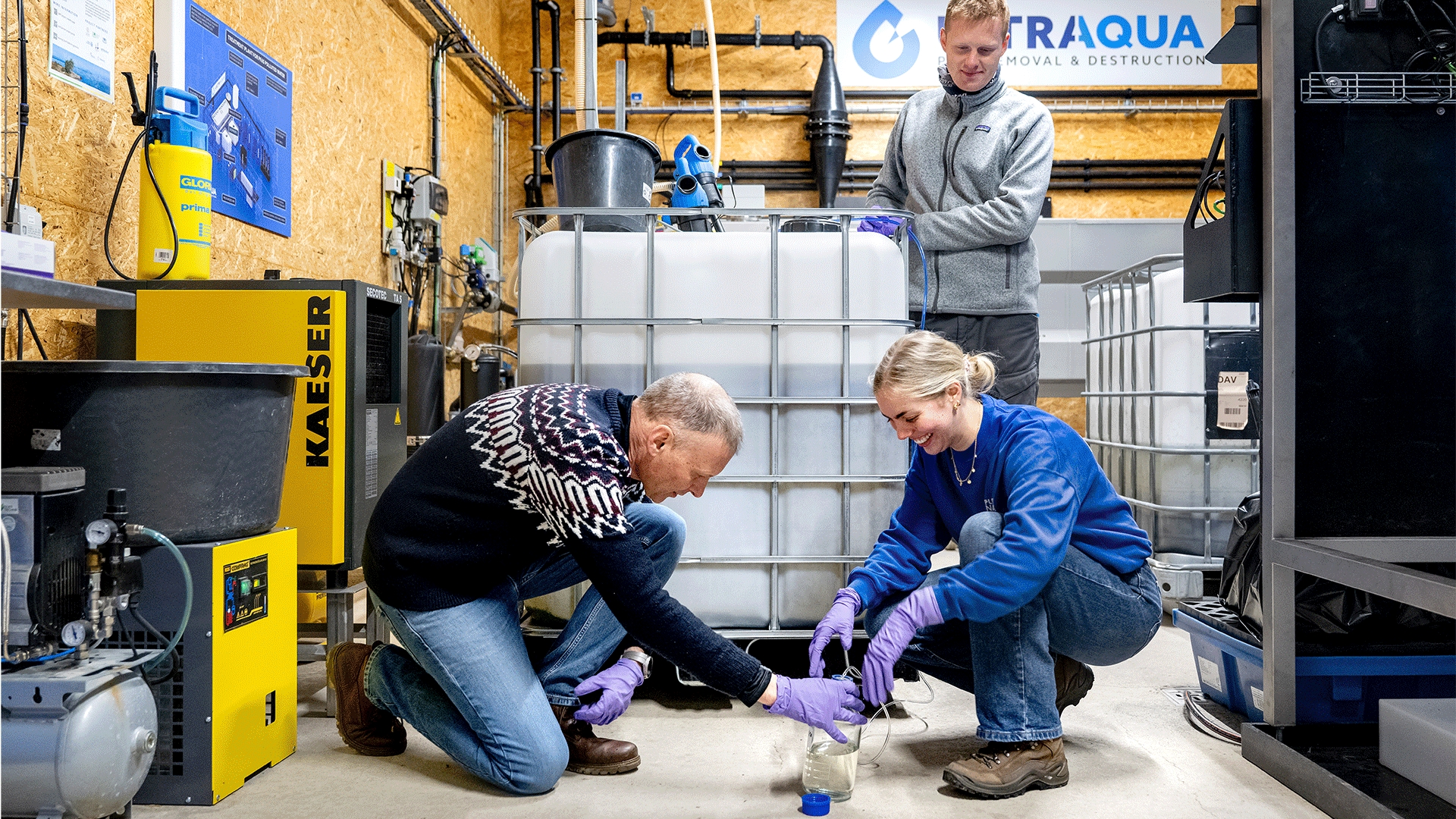 Tre mennesker i færd med at tappe en vandprøve fra en stor beholder.